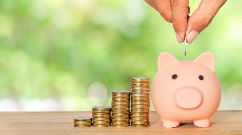money saving for business investment finance and banking concept. people hands putting coin to piggy bank and row of coin stack on wood table and green blur nature background.